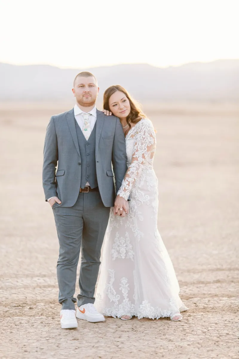 Bride in a long sleeve lace gown standing with her groom in a grey three piece suit