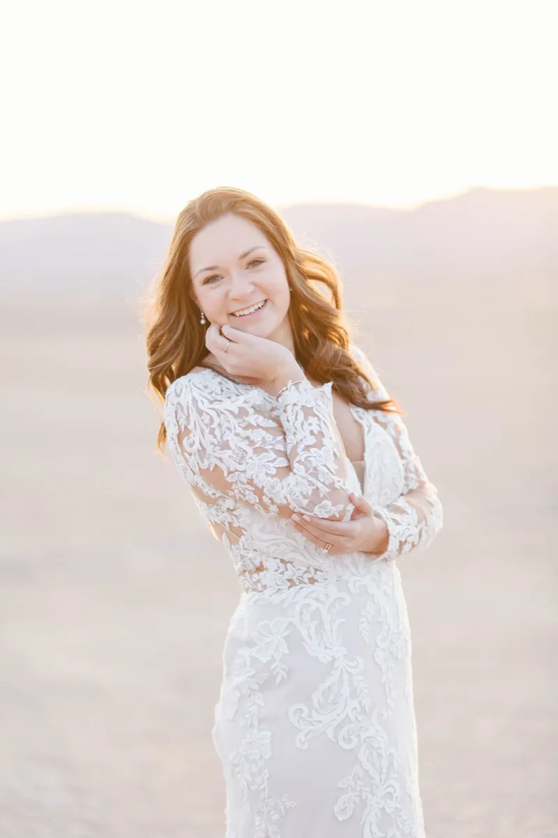 Red haired bride in a lace gown smiling back over her shoulder in the late sun