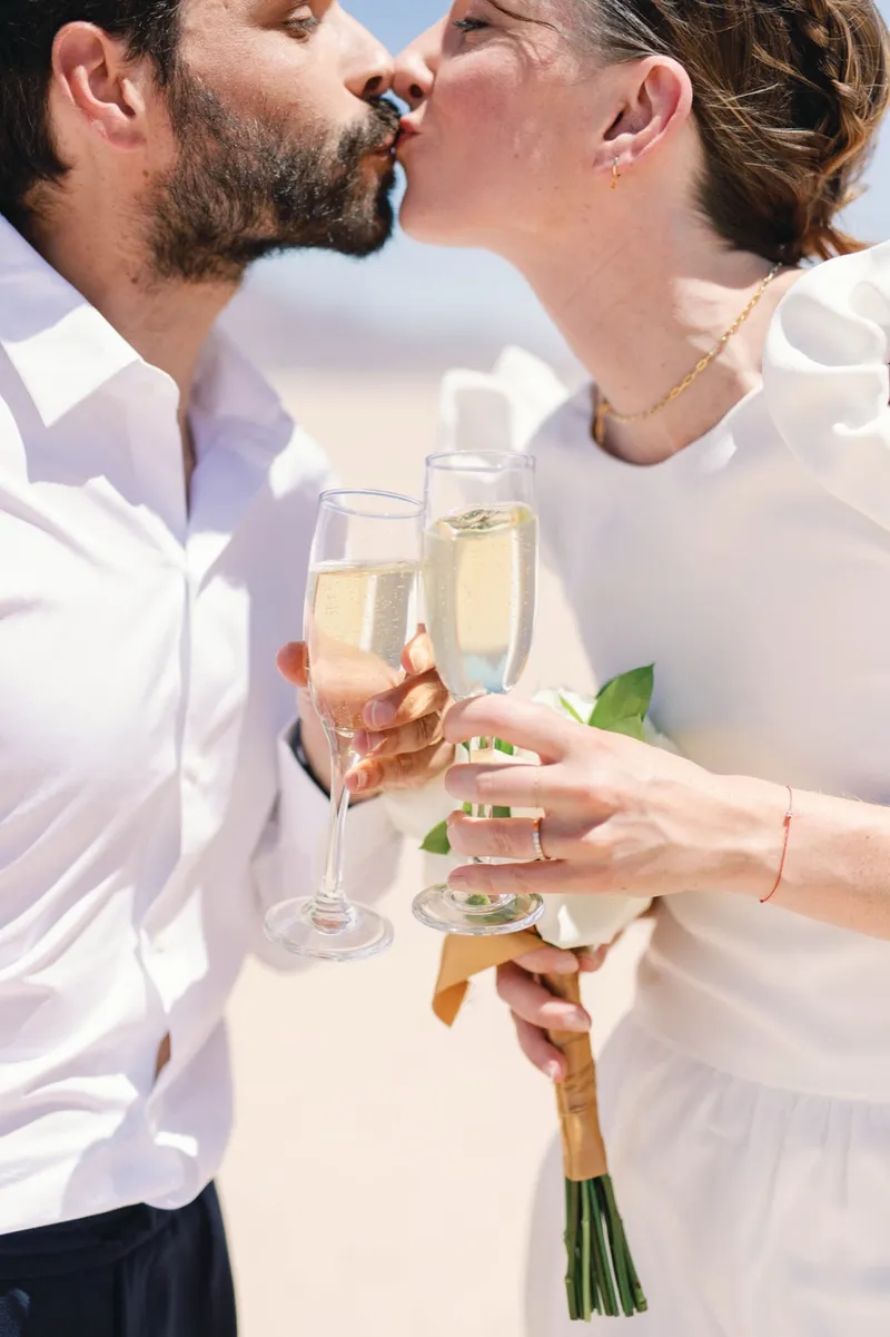 Couple clinking champagne glasses close to the camera with a bouquet resting between them