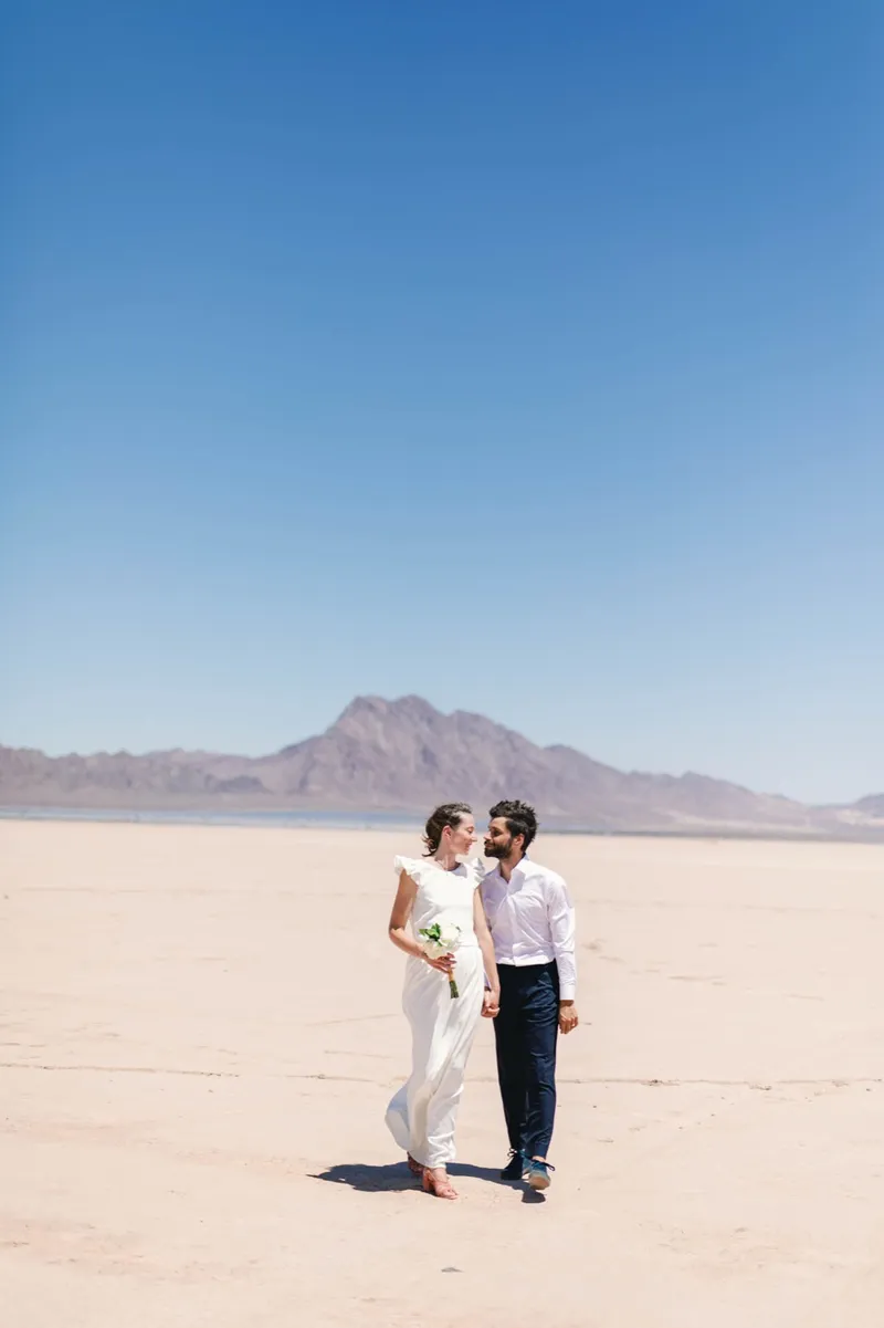 Bride and groom walking together across an enormous empty lake bed with a single peak on the horizon