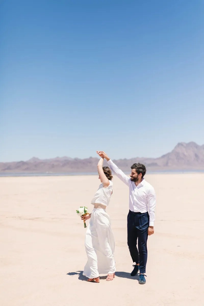 Groom spinning his bride under his arm with her bouquet in her free hand and mountains behind