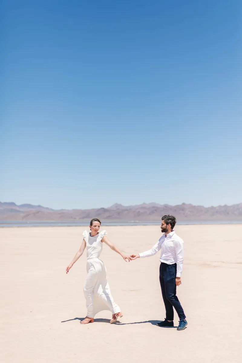 Bride and groom walking apart but hand in hand across the wide open flat