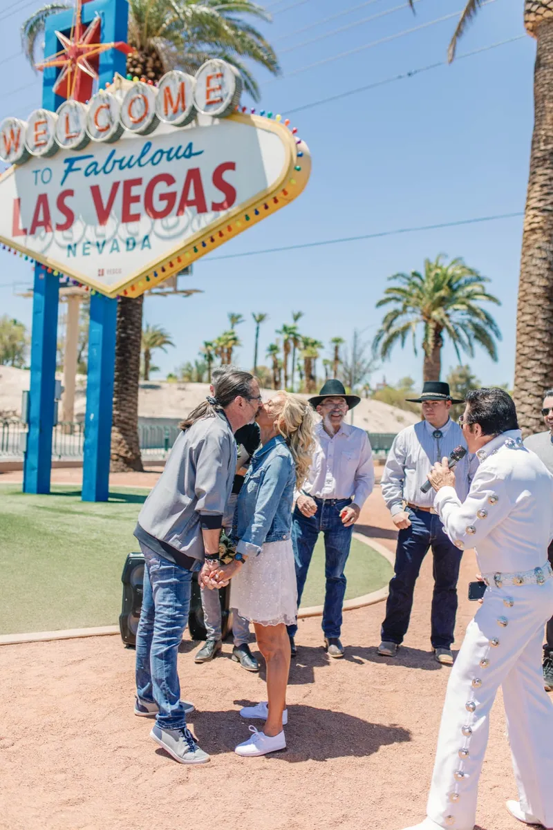 Couple holding hands during their vows while their guests watch beside the sign