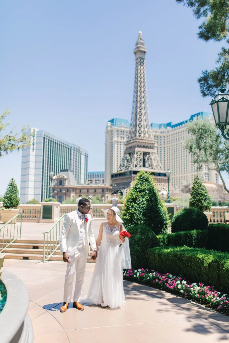 Wide photo of the couple standing small on the walkway while the Paris Las Vegas tower fills the sky