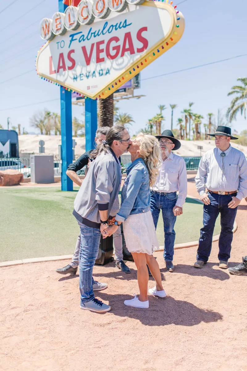 A couple kissing at the Welcome to Fabulous Las Vegas sign while an Elvis impersonator sings for their ceremony