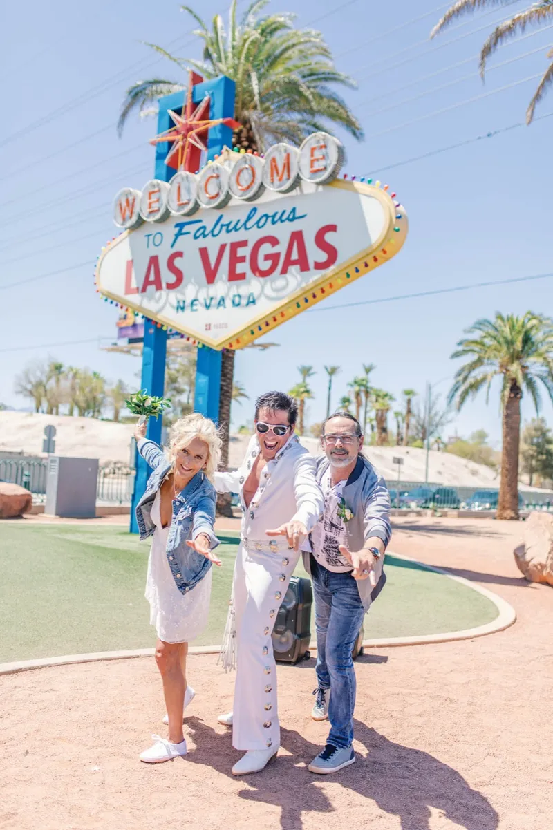 Elvis officiant with his arms out to the couple and their guests beside the sign