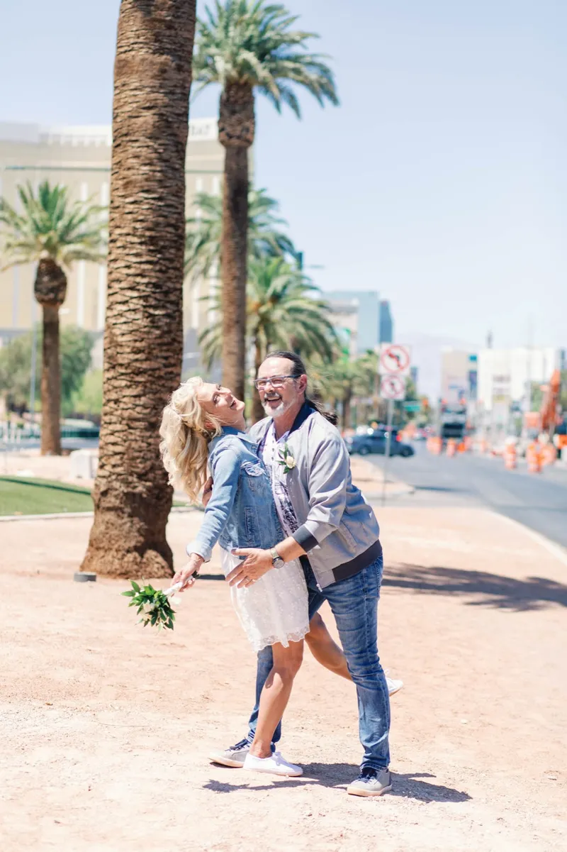 Bride leaning in to kiss her groom under a palm tree with her small bouquet in hand