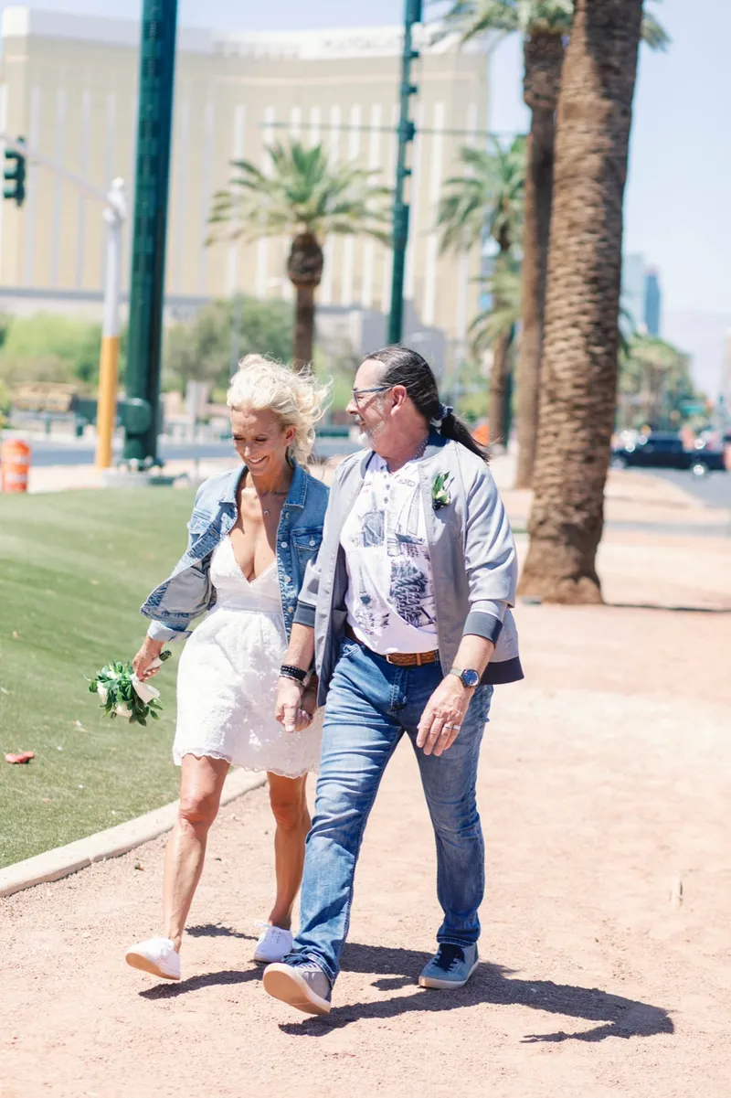Bride and groom walking arm in arm past the palms, both laughing