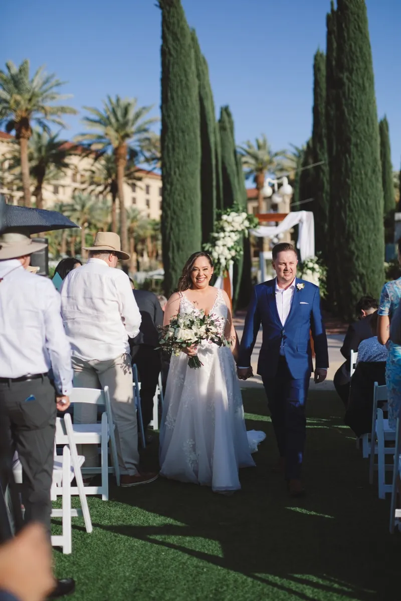 Bride and groom walking back up the aisle together past guests in white chairs after the ceremony