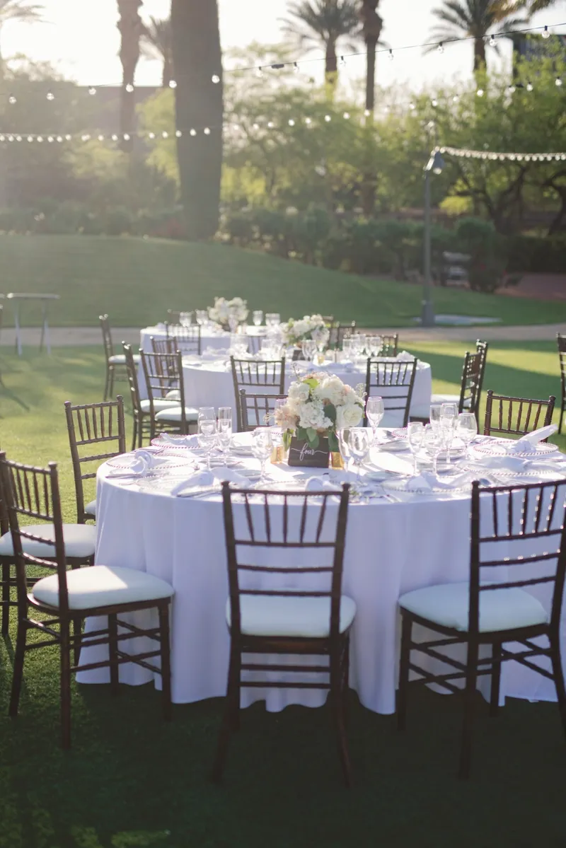 Reception tables laid out on the lawn under strung cafe lights with palms behind them