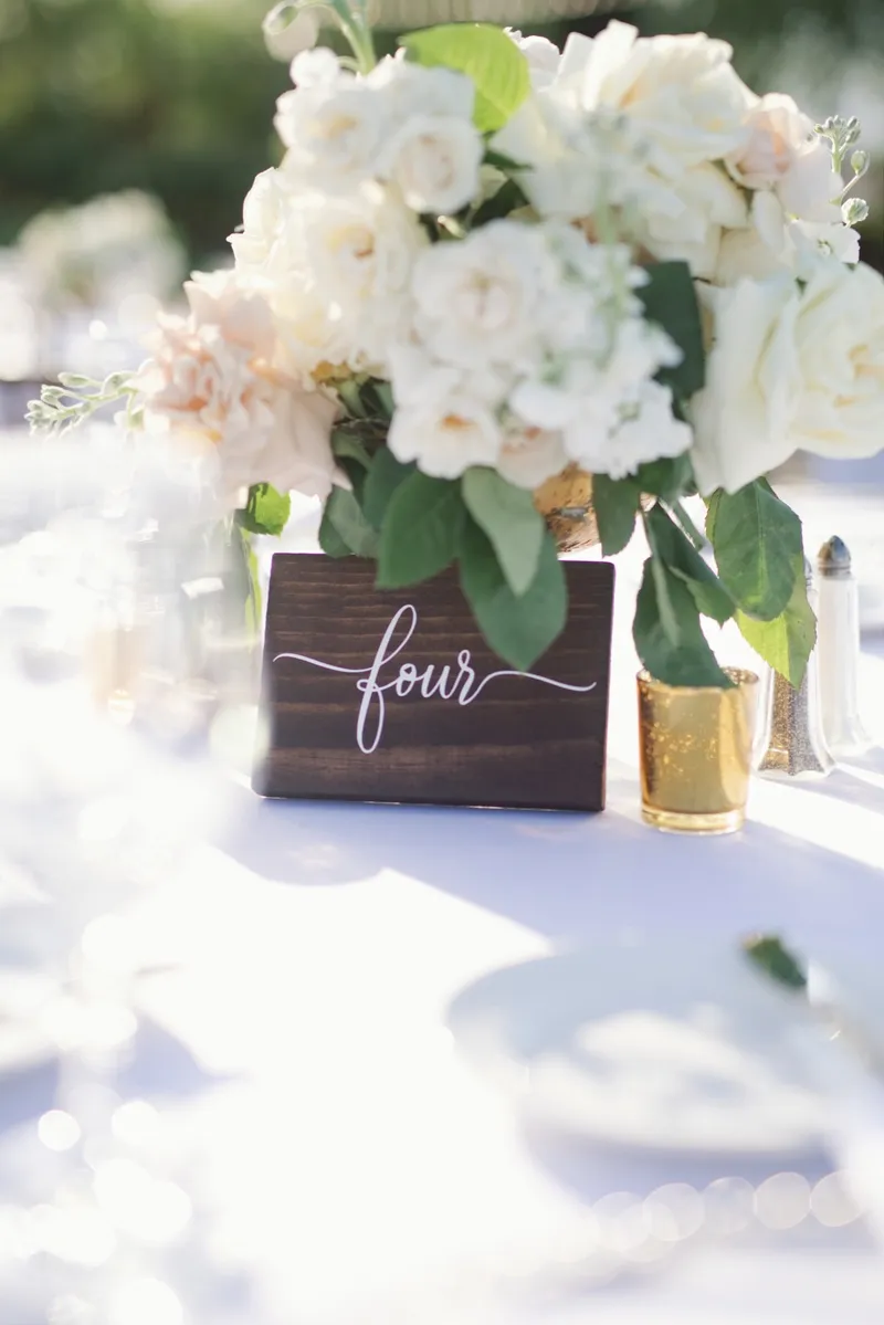 A wooden table number four propped against a white and blush centerpiece beside a gold votive