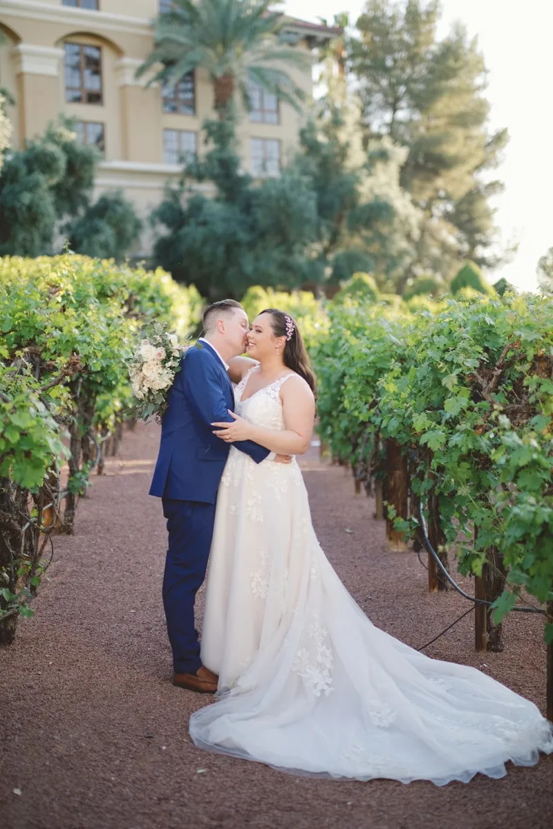 Bride and groom leaning into a kiss on the vineyard path with the resort building behind them
