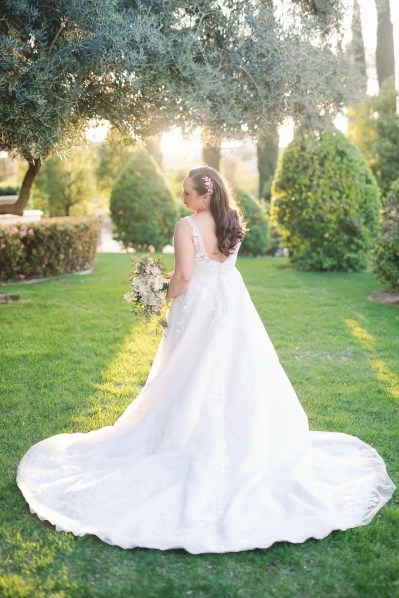 Bride standing on the grass with her train spread behind her, looking back over her shoulder in low sun