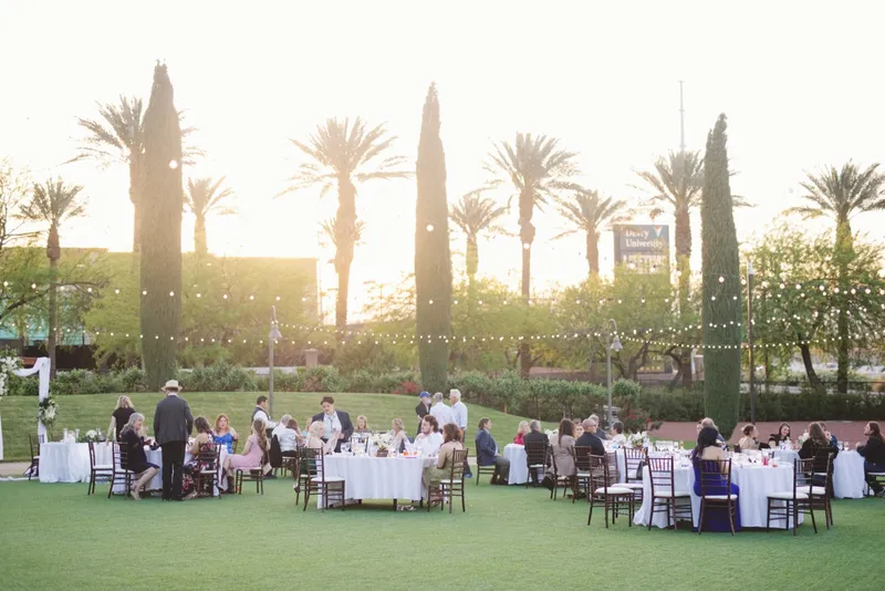 Guests seated at the lawn reception as the sun drops behind the palms and cypress