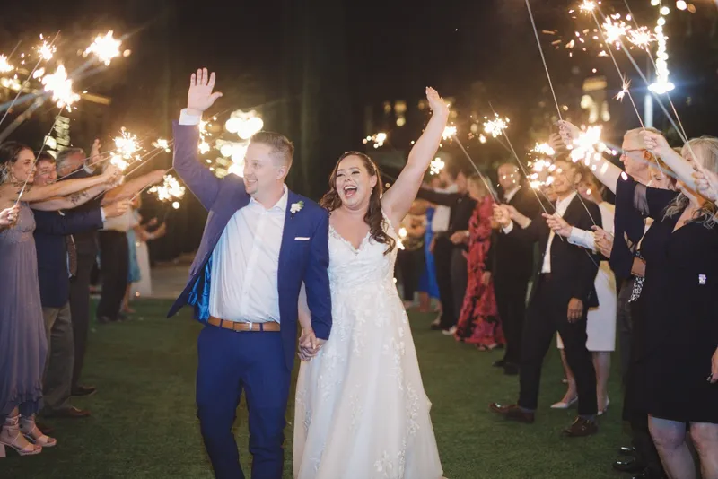 Newlyweds walking hand in hand through a tunnel of guests holding sparklers at night
