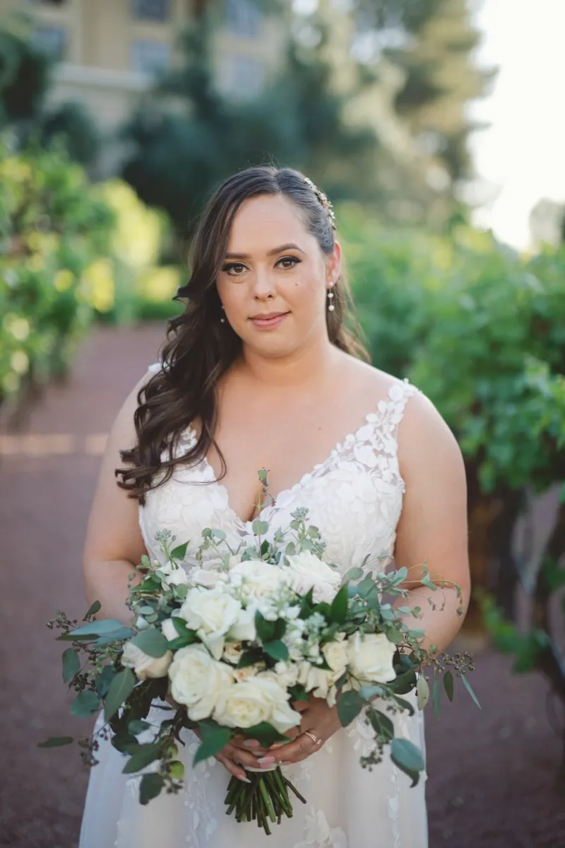 Bride holding a white and greenery bouquet with the vineyard rows behind her