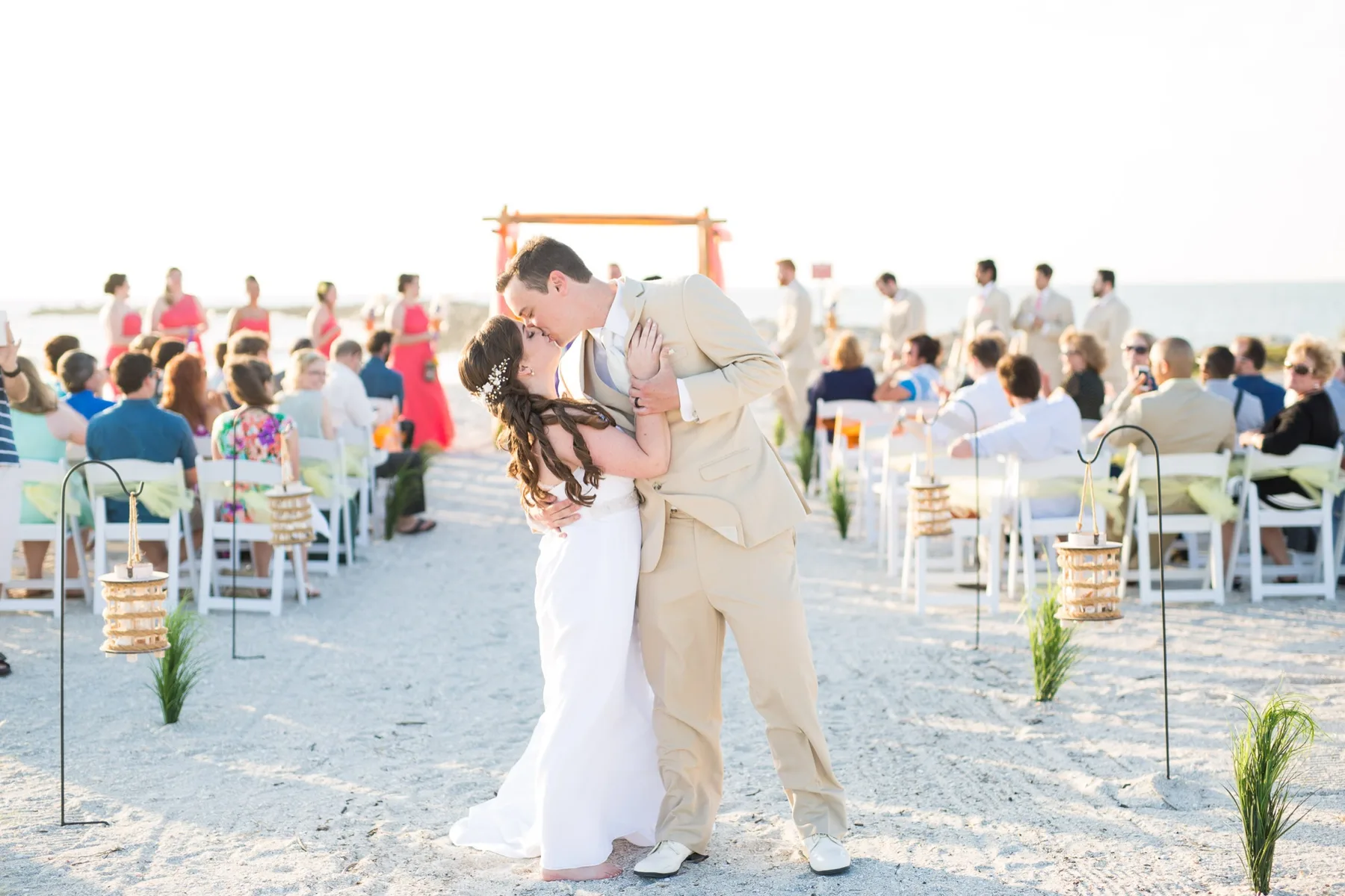 Bride and groom kissing at the end of a beach ceremony while their guests look on