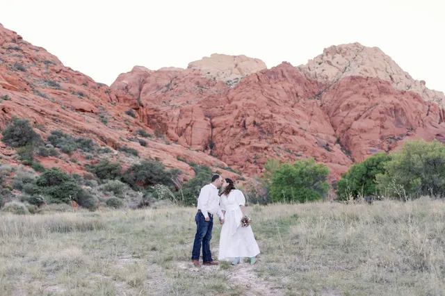 Bride and groom kissing in a grassy wash below the red sandstone cliffs of Red Rock Canyon after their elopement