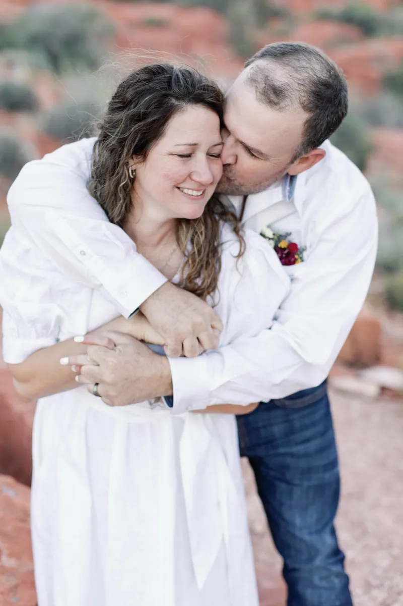 Bride smiling with her eyes closed as her groom holds her from behind