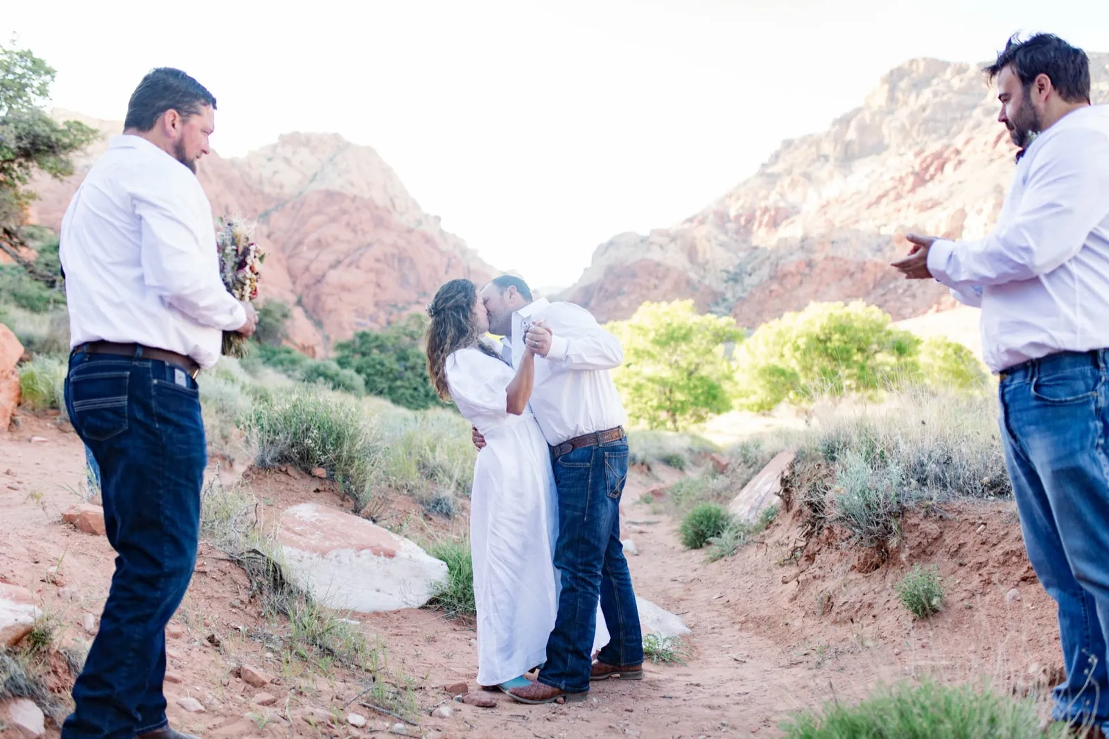 Couple kiss at the end of their Red Rock ceremony while two men from their small group stand at either side