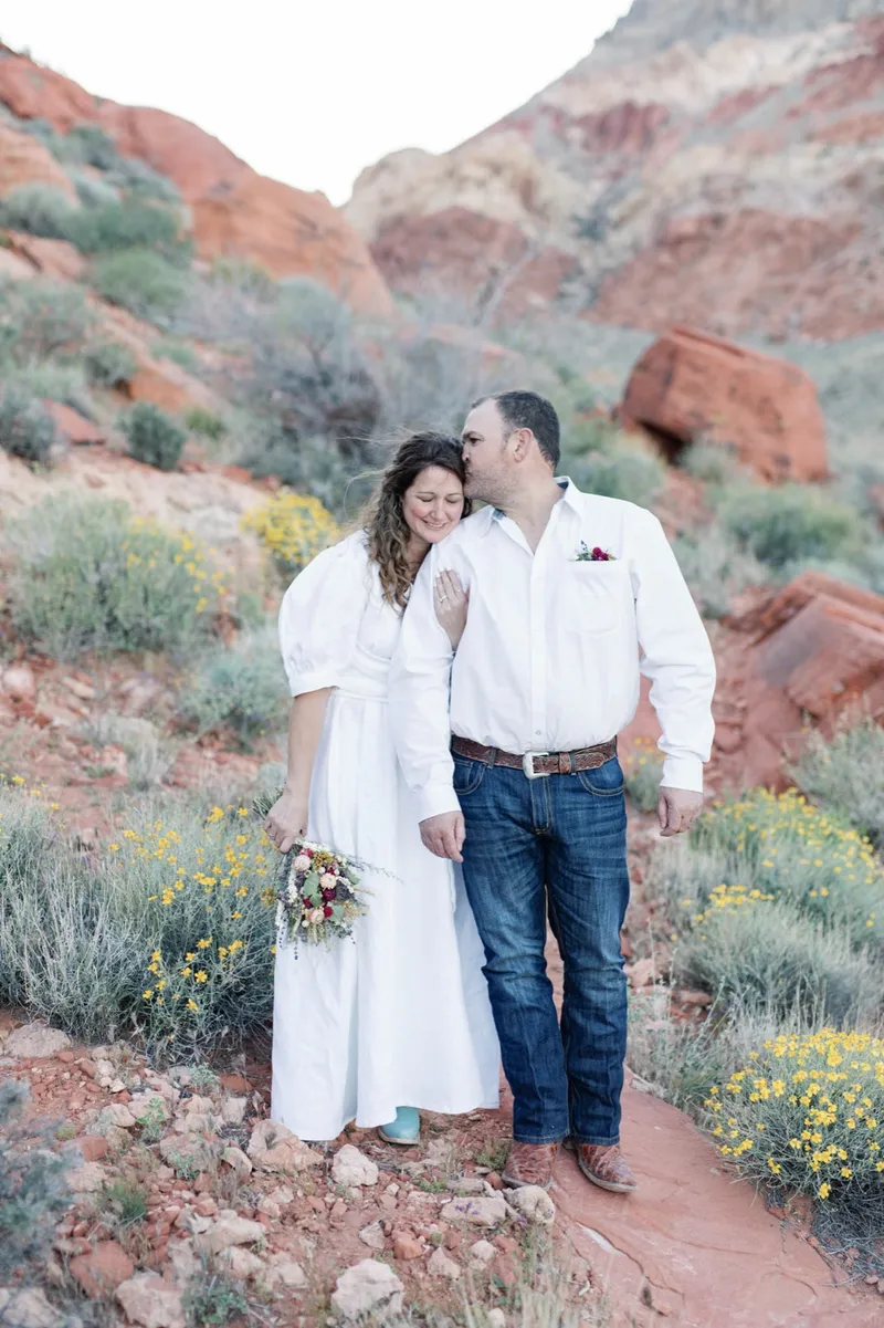 Bride and groom standing together in the sage with red rock formations behind