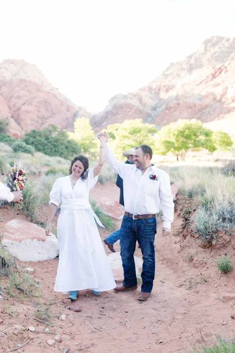 Groom raising his brides hand overhead as they walk through the brush together