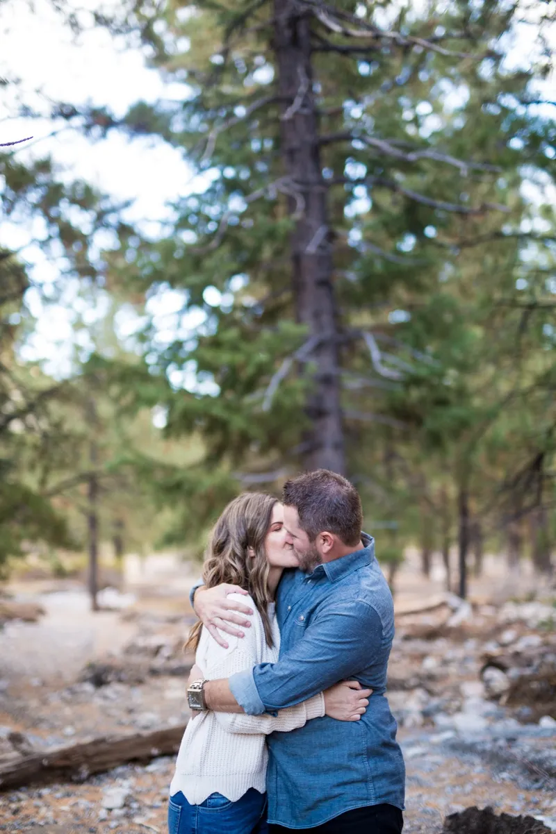 Couple holding each other in a clearing among tall pines with fallen logs on the ground