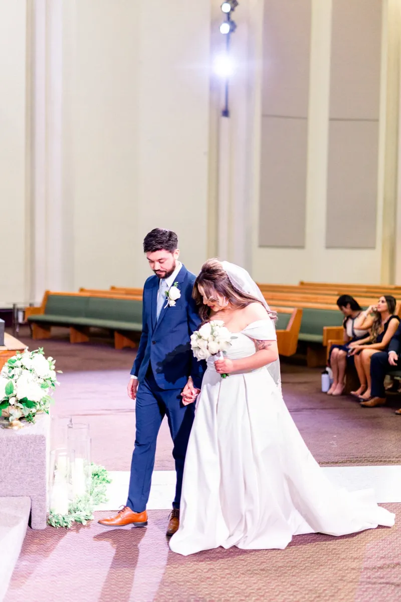 The couple coming back down the aisle, the bride leaning into the groom's shoulder with her bouquet in both hands