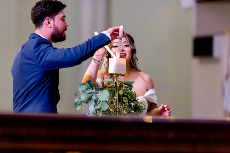 The groom holding a lit taper to the unity candle while the bride sits below him laughing with her eyes closed
