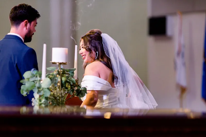 The bride laughing beside the unity candle with her veil over her shoulder, a thread of smoke still rising from the wick
