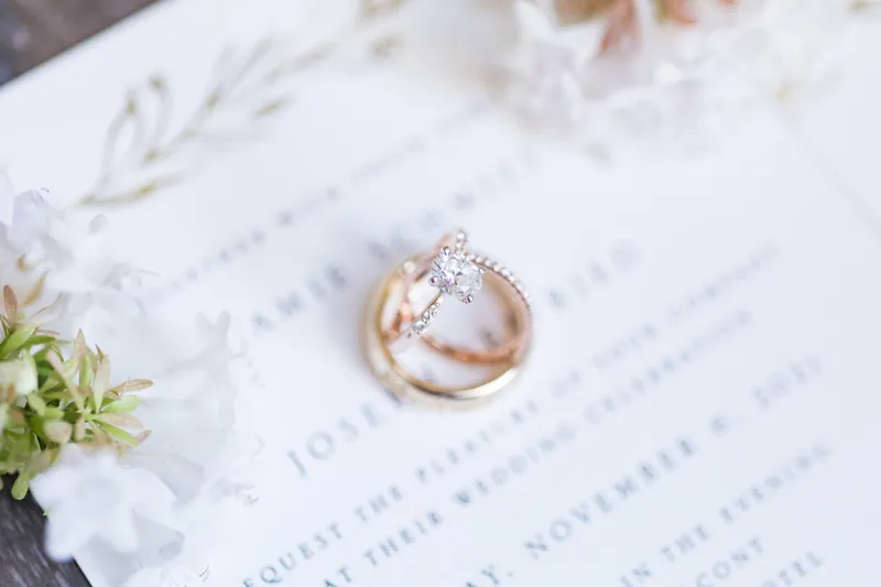 Close view of the engagement ring and both wedding bands resting on the invitation card