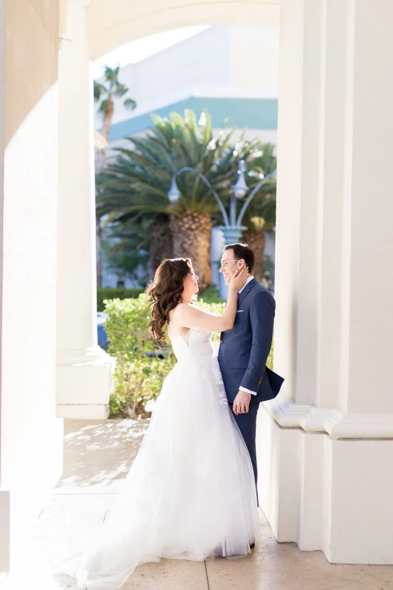 Bride and groom facing each other in a stone archway with palm trees behind them
