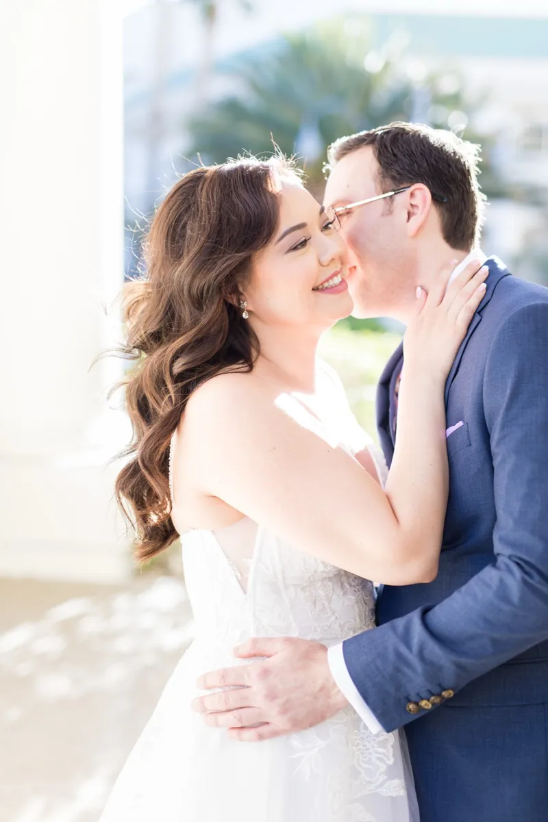 Close portrait of the groom kissing the bride's cheek while she laughs