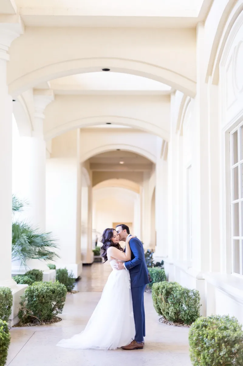 Bride and groom embracing at the far end of the long arched walkway