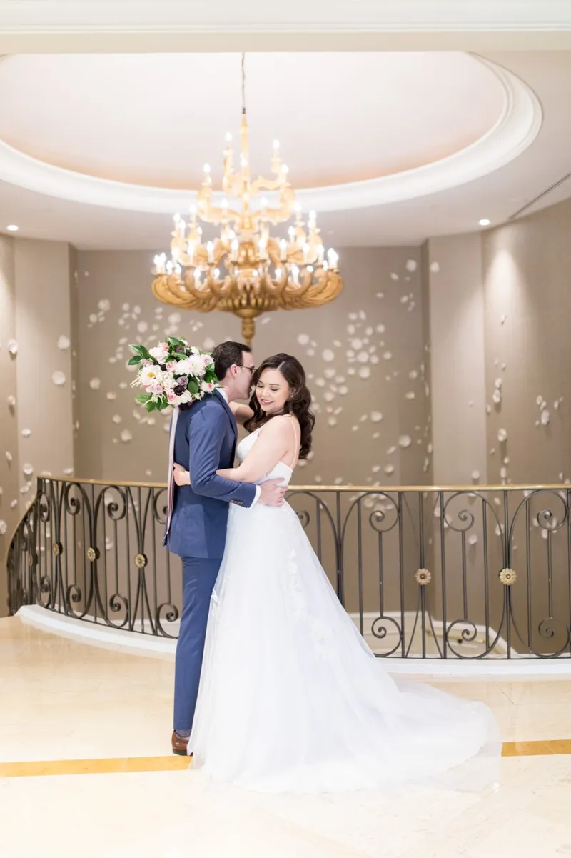Bride and groom embracing on the marble stair landing under a gold chandelier