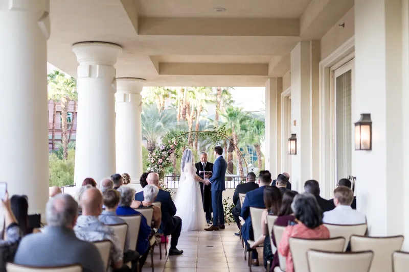 Ceremony under way on the covered balcony with guests seated in rows and palms beyond the railing
