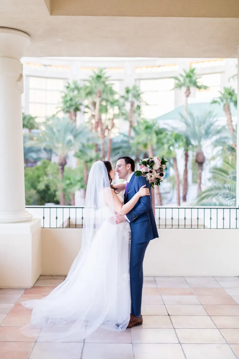 Bride and groom holding each other in front of the circular floral arch, her veil trailing on the tile