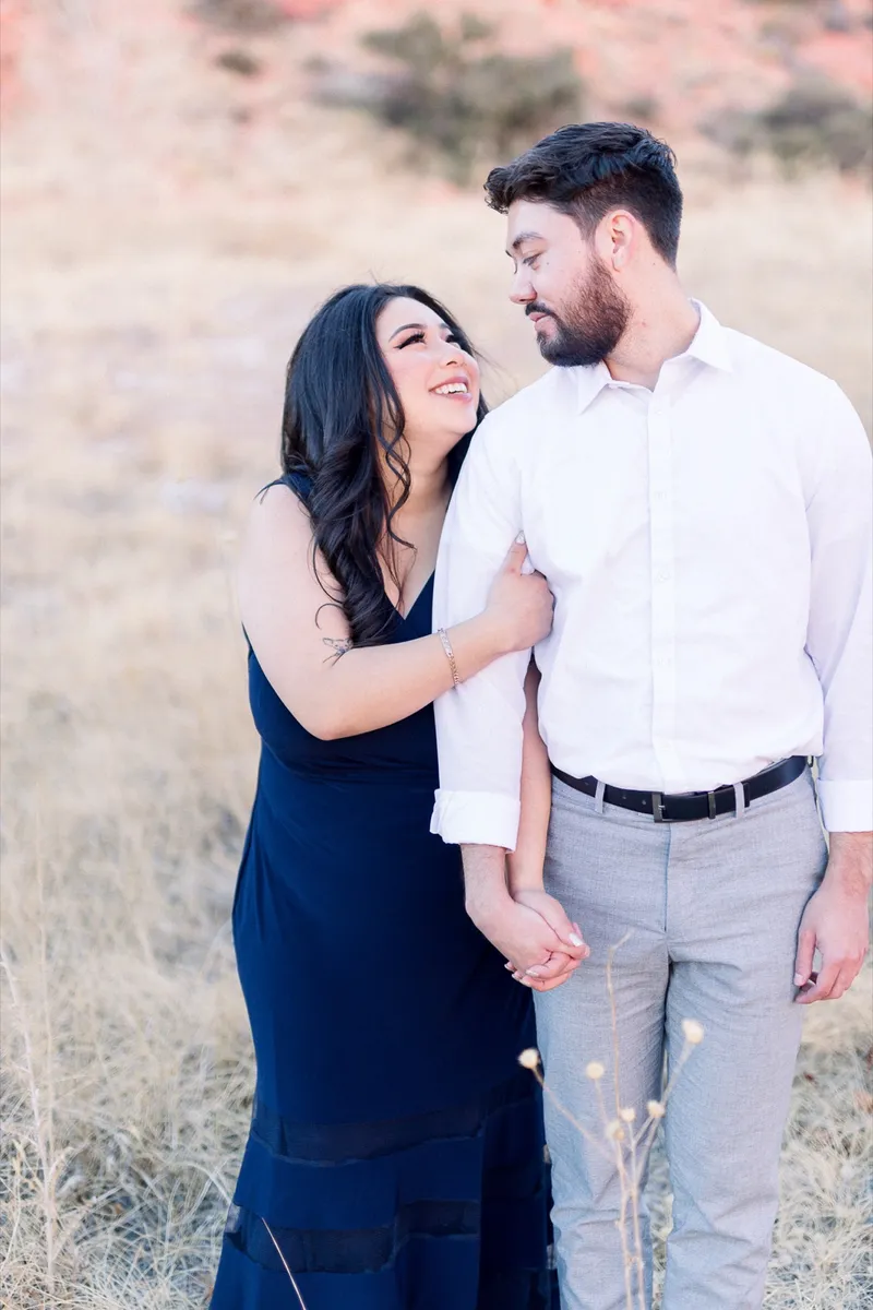 Couple standing together and laughing with her hand on his chest in low desert light