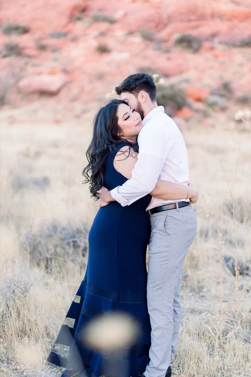 Woman in navy resting against her fiance's chest with desert brush all around them