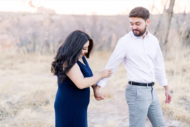 Man leading his fiancee by the hand along a dirt path with her navy dress trailing behind her