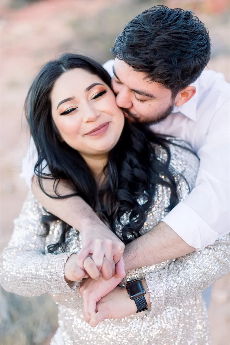 Man wrapping his arms around his fiancee from behind as she rests her hands on his