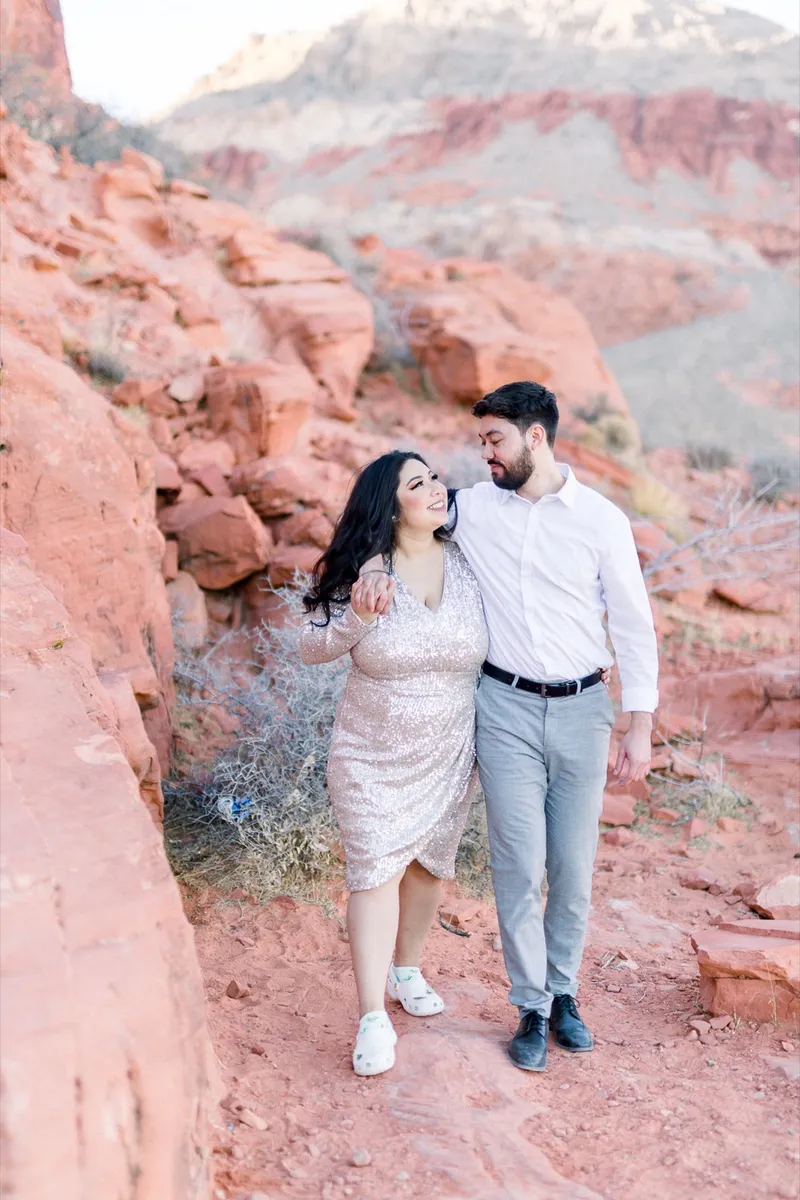 Couple walking a red sandstone ledge together, her in a sequin dress and white sneakers