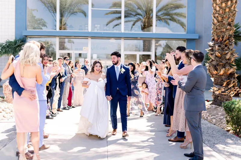 The couple walking out through two lines of guests on the sidewalk in front of the church's blue glass windows