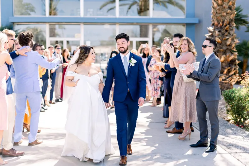 Guests cheering and holding up phones as the couple come through the send off line under the palms