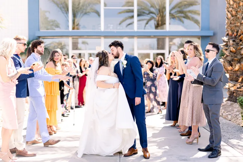 The couple stopping to kiss in the middle of the send off line while their guests clap around them