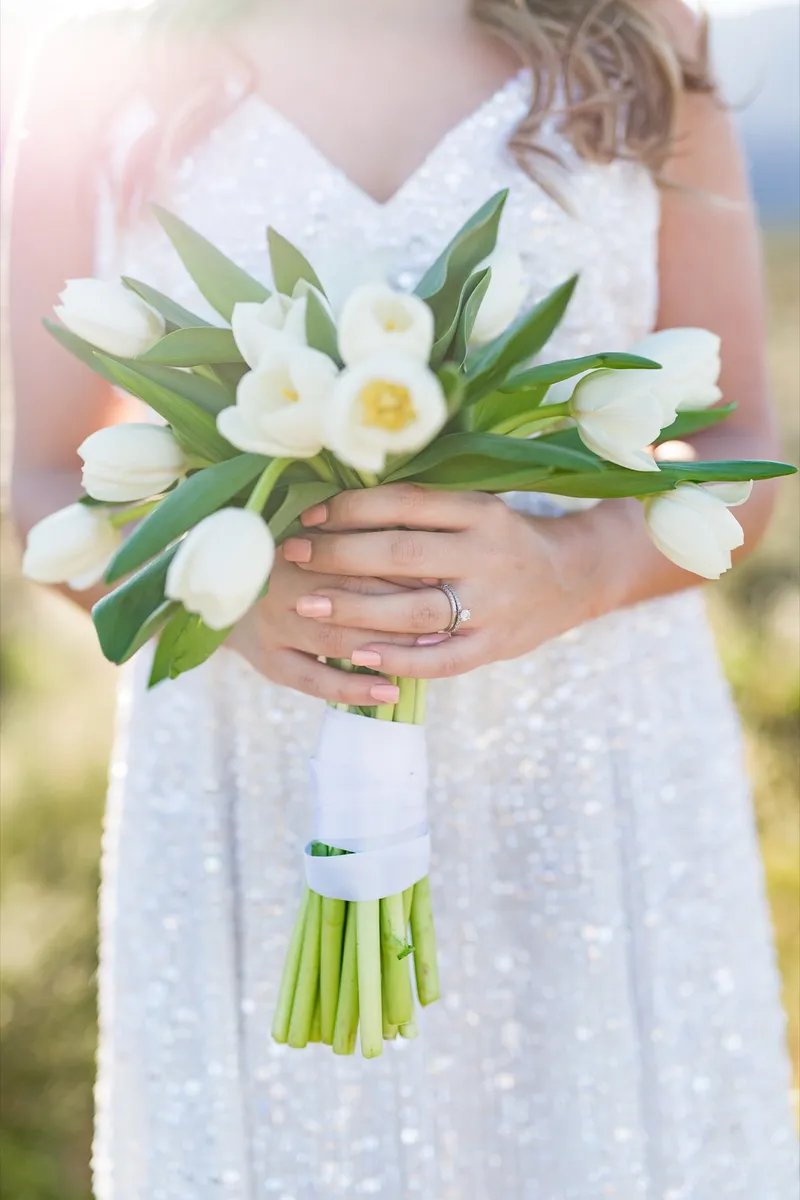 Close view of a bouquet of white tulips held against a beaded white dress