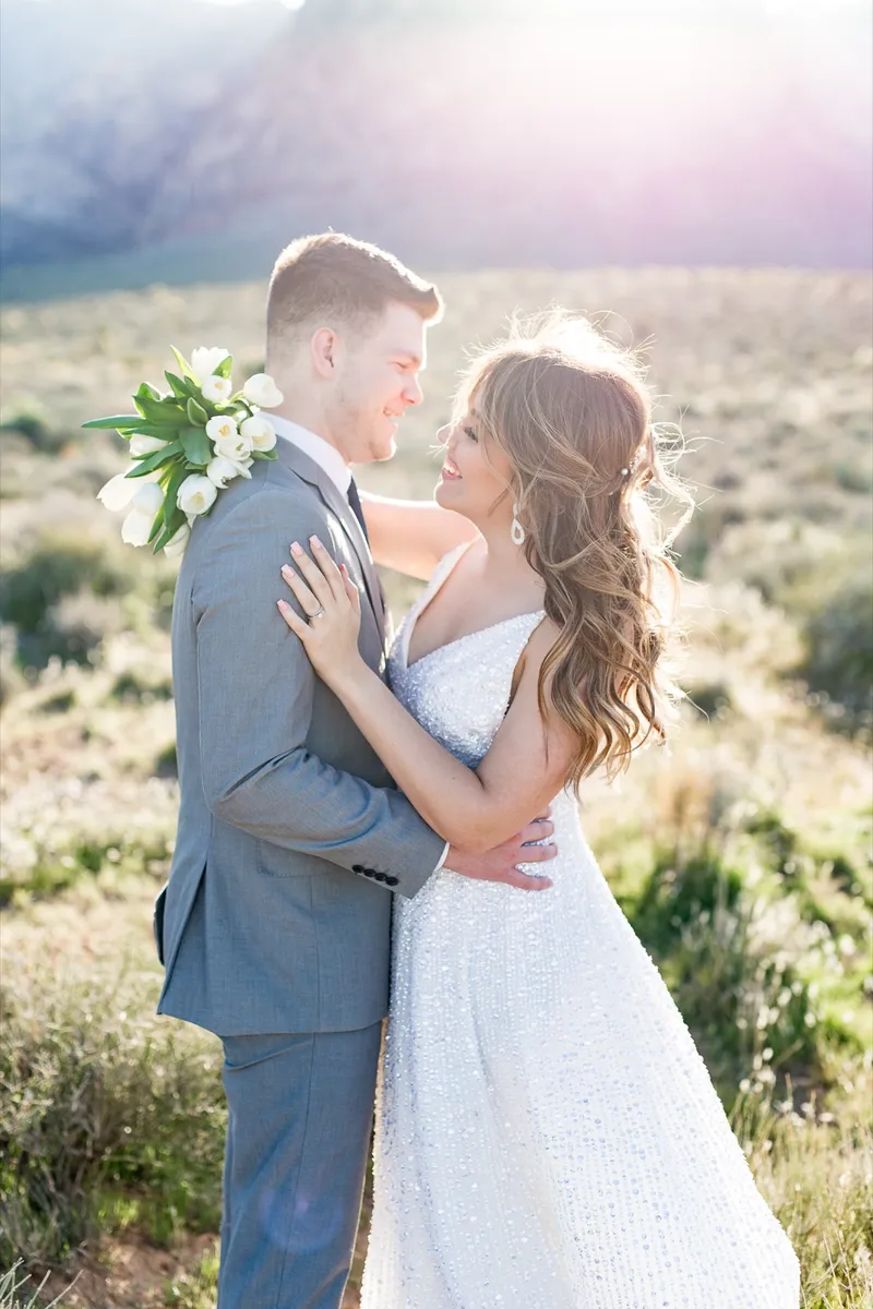 Bride holding white tulips against her groom's shoulder as they stand close together