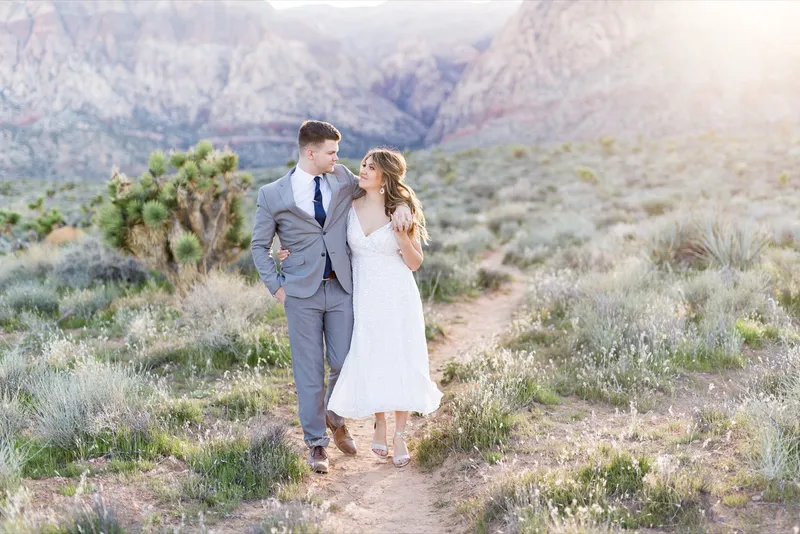 Couple standing close among joshua trees with the layered ridge line behind them