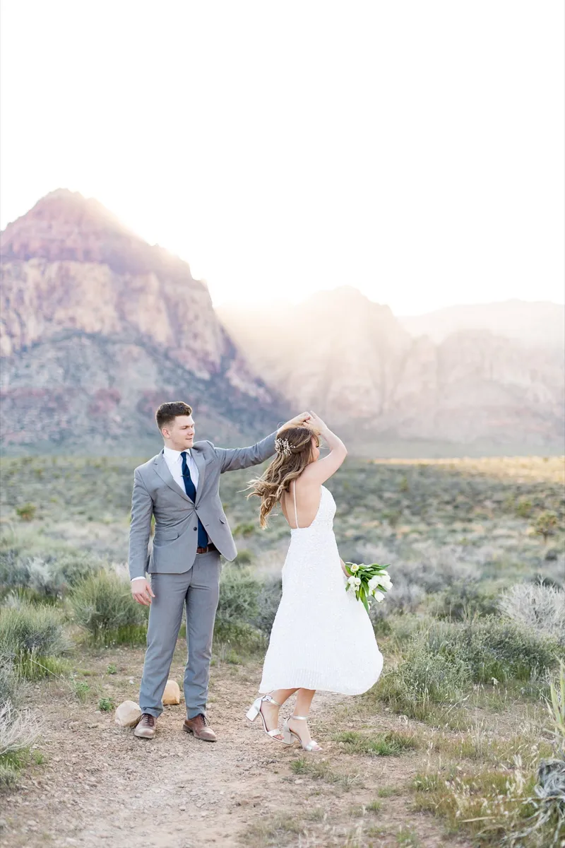 Groom lifting his brides hand as she turns and laughs on the desert flat