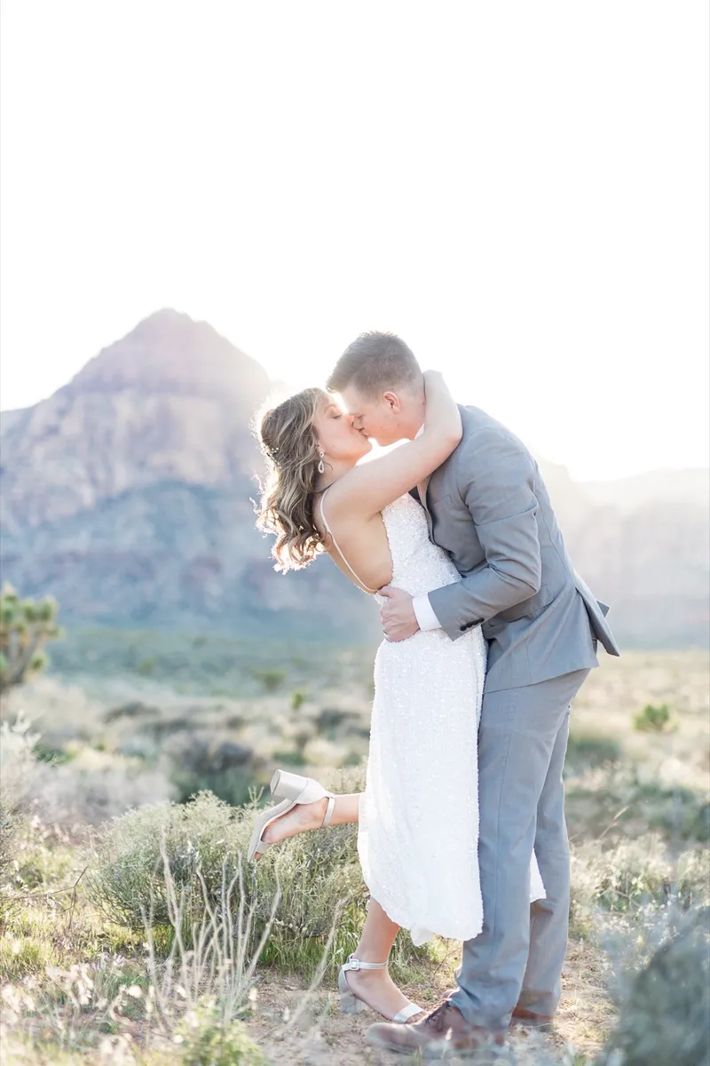 Couple kissing with the mountain rising behind and dry grass around them
